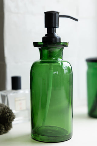 The Apothecary-Style Green Glass Soap Dispenser - 300ml with other bathroom accessories in the background.