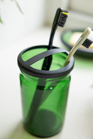 Close-up of the Apothecary-Style Green Glass Toothbrush Holder with toothbrushes inside.