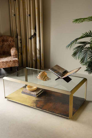 The Art Nouveau Coffee Table styled with a shell, books, a book stand and a bowl. There is a leopard print chair, curtain and a plant also in the background.