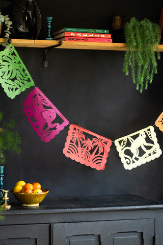 The Assorted Colourful Paper Garland hanging from shelf on a black wall above a sideboard, styled with home accessories, fruit and plants.