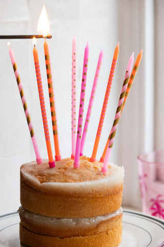 The Assorted Pink Cake Candles - Pack Of 10 styled on a cake, with a match lighting some of the candles.