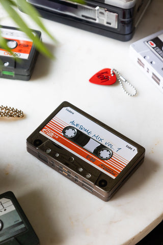 The Awesome Mix Cassette Tape Storage Tin with the lid on, styled on a white surface with other tins and some small accessories.