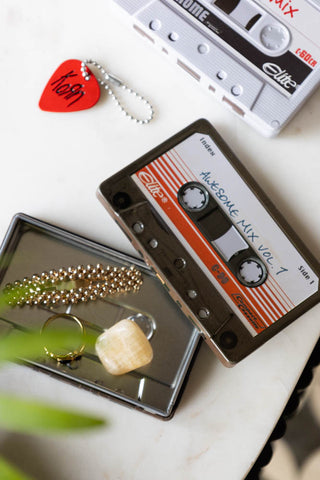 The Awesome Mix Cassette Tape Storage Tin with the lid off, seen from above styled on a white surface with another storage tin and various accessories.