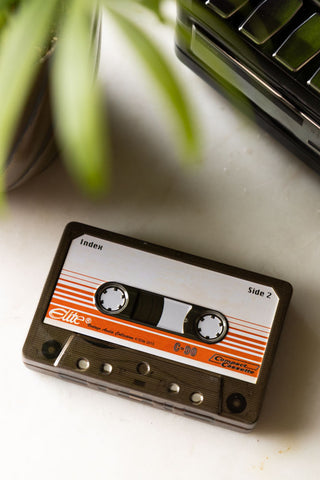 The reverse side of the Awesome Mix Cassette Tape Storage Tin seen from above, styled on a white surface with another tin and a potted plant.