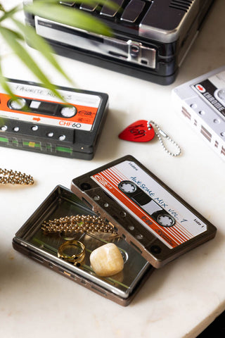 The Awesome Mix Cassette Tape Storage Tin with the lid off and various accessories inside, styled with other storage tins and a plant.