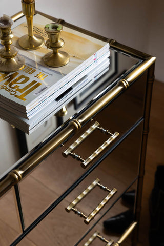 The corner of the Mirrored Bamboo Effect Chest Of Drawers seen from above, styled with magazines and candlestick holders on.