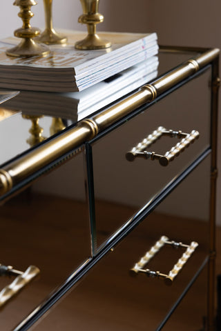 Close-up of the Mirrored Bamboo Effect Chest Of Drawers with magazines and candlestick holders styled on top.