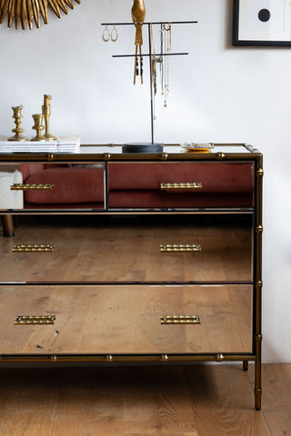 Close-up of the Mirrored Bamboo Effect Chest Of Drawers seen from the front, styled with various home accessories on top and on the wall.