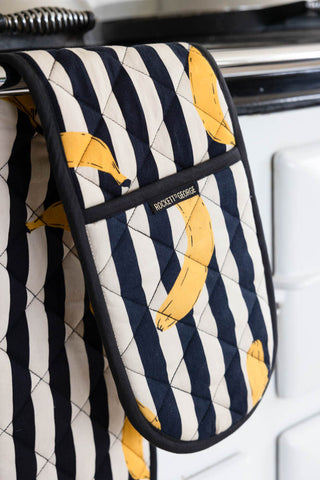 Close-up of the Banana Black & White Stripe Oven Gloves displayed hanging from a rail on the front of an oven.