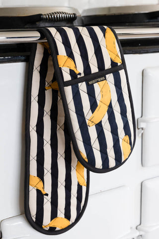 The Banana Black & White Stripe Oven Gloves styled hanging from a rail on the front of an oven.