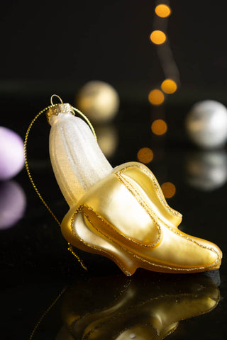 The Banana Christmas Tree Decoration styled on a dark surface with baubles and fairy lights in the background.