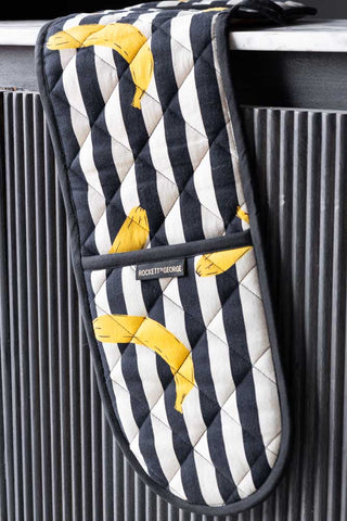 The Banana Black & White Stripe Oven Gloves styled across the edge of a table.