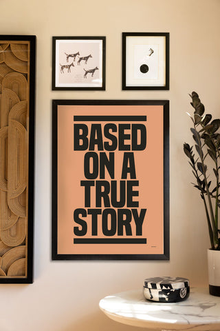 The Based On A True Story Art Print - Unframed, styled in a frame on a neutral wall with other art prints, above a table with a trinket box and a potted plant on.