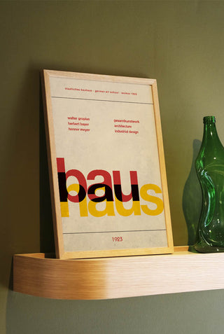 The Bauhaus Art Print styled in a frame, displayed leaning against the wall on a shelf next to a vase.