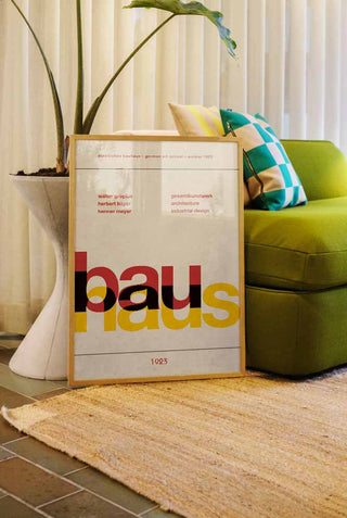 The Bauhaus Art Print styled in a frame, leaning against a sofa and a plant in a living room.