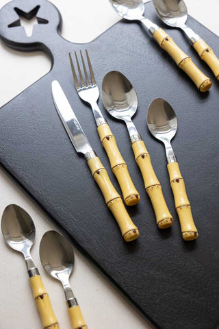 The Beautiful 16-Piece Bamboo Design Cutlery Set on a black serving board, displayed on a white table.