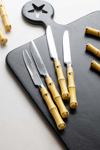 The knives from the Beautiful 16-Piece Bamboo Design Cutlery Set, displayed on a black serving board, with the handles of other pieces of cutlery also in the shot.