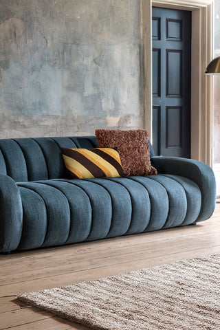 The Beautiful Blue Roll Back 3-Seater Sofa styled with some cushions on, next to a rug and a floor lamp.