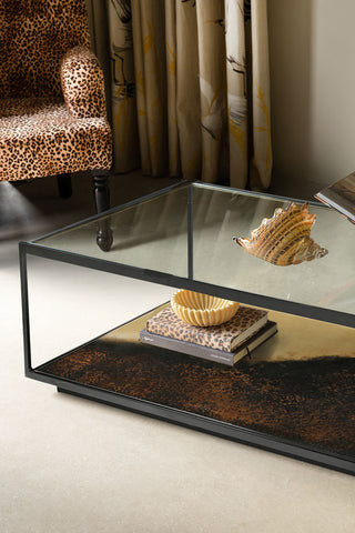 Close-up of the Beautiful Burnished Metal & Glass Coffee Table with various accessories on, with a chair and curtain in the background.