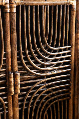 A bohemian-inspired rattan storage cabinet with a rich dark brown finish, featuring elegant arched patterns on the doors, styled with books, a lamp, and decorative accessories.