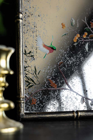 Close-up of the bottom left-hand corner of the Beautiful Pink Chinoiserie Decorative Mirror, styled on a black sideboard with a candlestick holder.