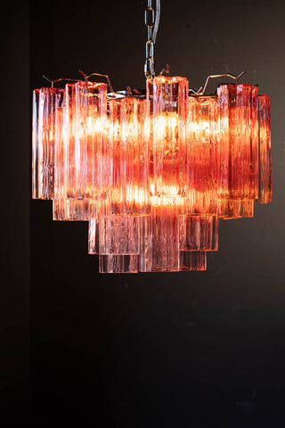 The Beautiful Waved Glass Chandelier in Pink switched on, in front of a dark wall.