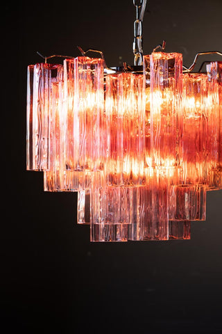 Close-up of the illuminated Beautiful Waved Glass Chandelier in Pink in front of a dark wall.