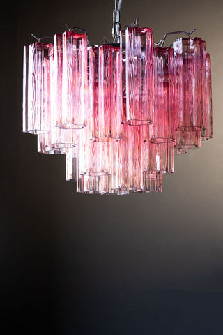 The Beautiful Waved Glass Chandelier in Pink displayed hanging in front of a dark wall.