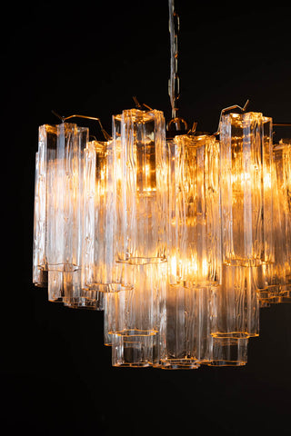 Close-up of the illuminated Beautiful Waved Glass Chandelier in Clear in front of a dark wall.