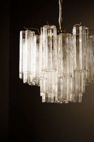 The Beautiful Waved Glass Chandelier in Clear hanging in front of a black wall.