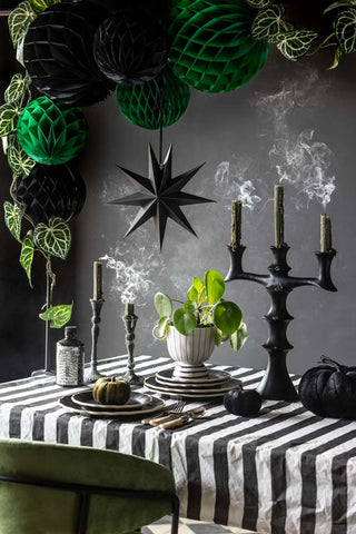 Black honeycomb balls styled on a table clamp with deep green honeycomb paper decorations. On the table is styled candlesticks, plates, pumpkins and beetlejuice inspired pieces.