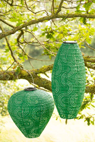 The Bell Shaped Green Outdoor Garden Lantern styled next to a similar lantern hanging on a branch.