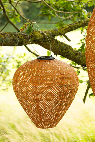 The Bell Shaped Ochre Outdoor Garden Lantern shown hanging on a branch.