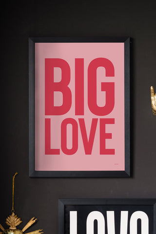 The Big Love Red & Pink Art Print - Unframed, styled in a black frame on a black wall with another art prints and some ornaments.