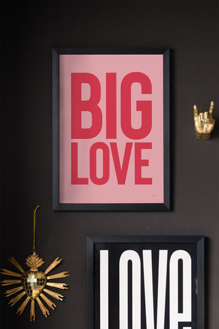 The Big Love Red & Pink Art Print - Unframed displayed in a black frame, styled on a black wall with another art print and two ornaments.