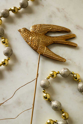 The Bird Christmas Tree Topper styled on a white marble surface with some decorative beads.