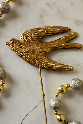 The Bird Christmas Tree Topper styled on a marble surface with some bead decorations.