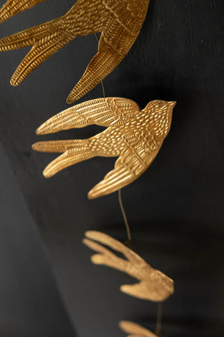 Close-up of the Pretty Gold Birds Garland on a black wall.