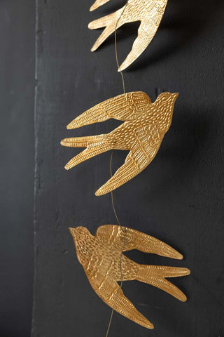 The Pretty Gold Birds Garland hanging in front of a black wall.