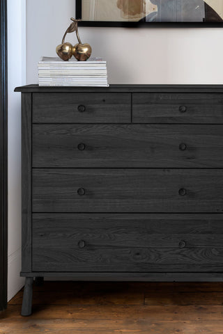 Close-up of the Black 5-Drawer Chest styled with a stack of magazines and a golden cherries ornament on top.