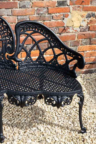 Close-up of the Black Antique-Style Garden Bench in front of a brick house in the background.