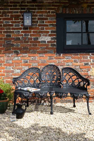 The Black Antique-Style Garden Bench styled outdoors in front of a brick house.