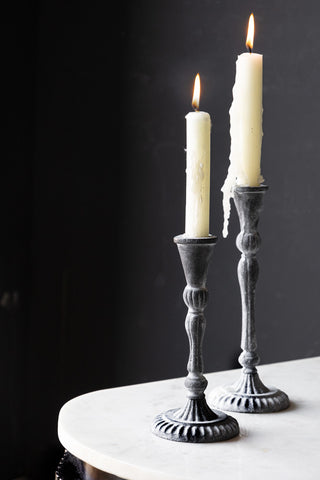 The Short and Tall Black Antique Zinc Style Candlestick Holders styled together on a white surface with lit candles inside.