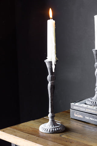 The Tall Black Antique Zinc Style Candlestick Holder styled with a lit candle inside, with the short version and some books in the background.