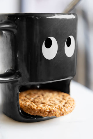 Close-up of the black cookie holding face mug. The eyes are looking up to the top left hand corner. In the cookie compartment is a oat biscuit.