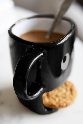 Side angle of the black handle of the black mug. The face mug has a compartment to hold a biscuit.