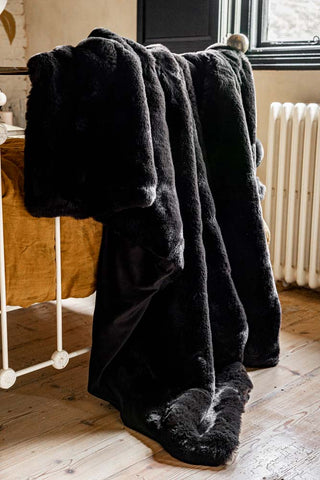 The Black Faux Fur Throw draped across the end of a bed.