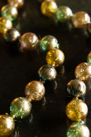 Close-up of the Black, Green & Gold Bauble Garland displayed on a dark surface.