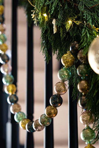 The Black, Green & Gold Bauble Garland styled on a styled stairs with greenery and fairy lights