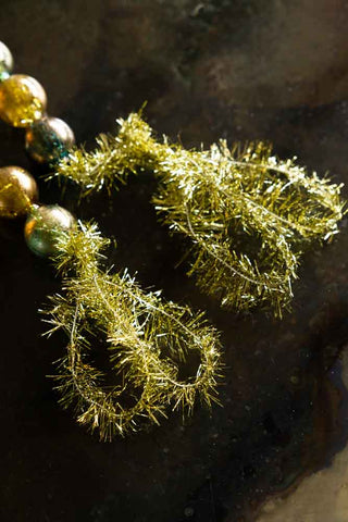 Close-up of the ends of the Black, Green & Gold Bauble Garland displayed on a dark surface.